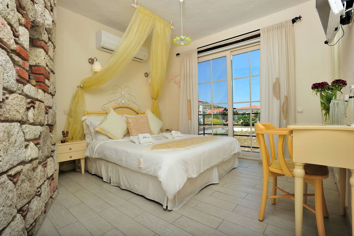 A bedroom with a bed, a bedside table, a chair, a window with curtains, and a view of the outside.