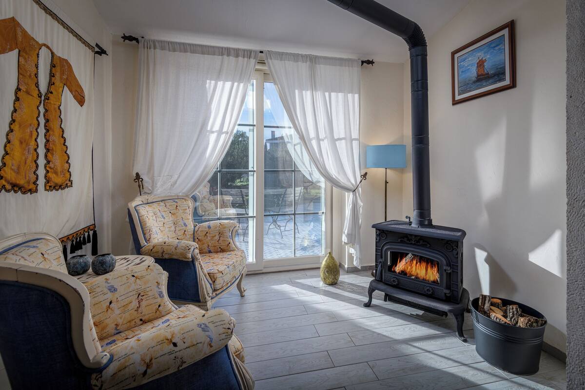 A cozy living room with a fireplace, patterned furniture, and a large window with curtains.