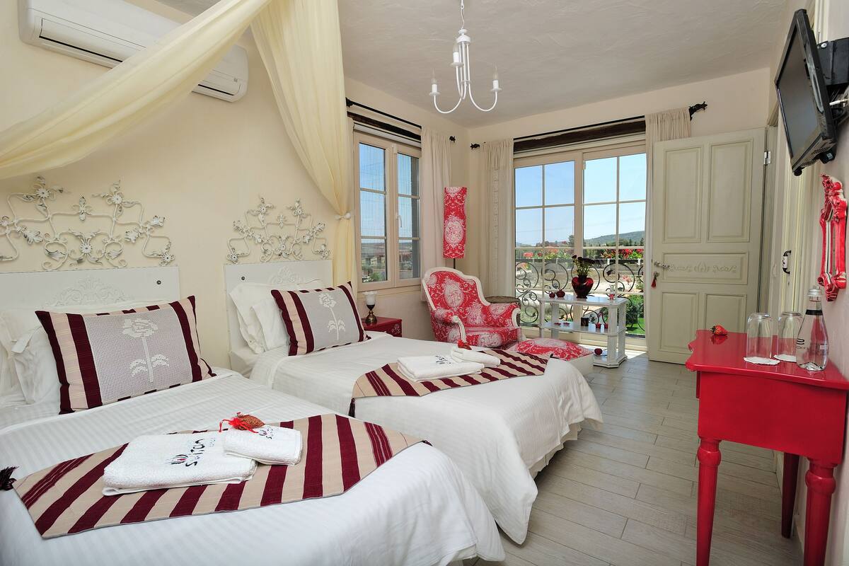 A hotel room with two beds, a red table, and a balcony with a view.