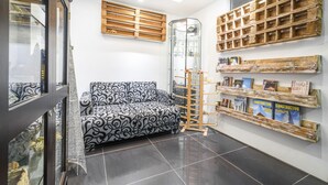 Een moderne woonkamer met een gestreept bankje, houten planken met boeken en een glazen deur die naar een andere kamer leidt.