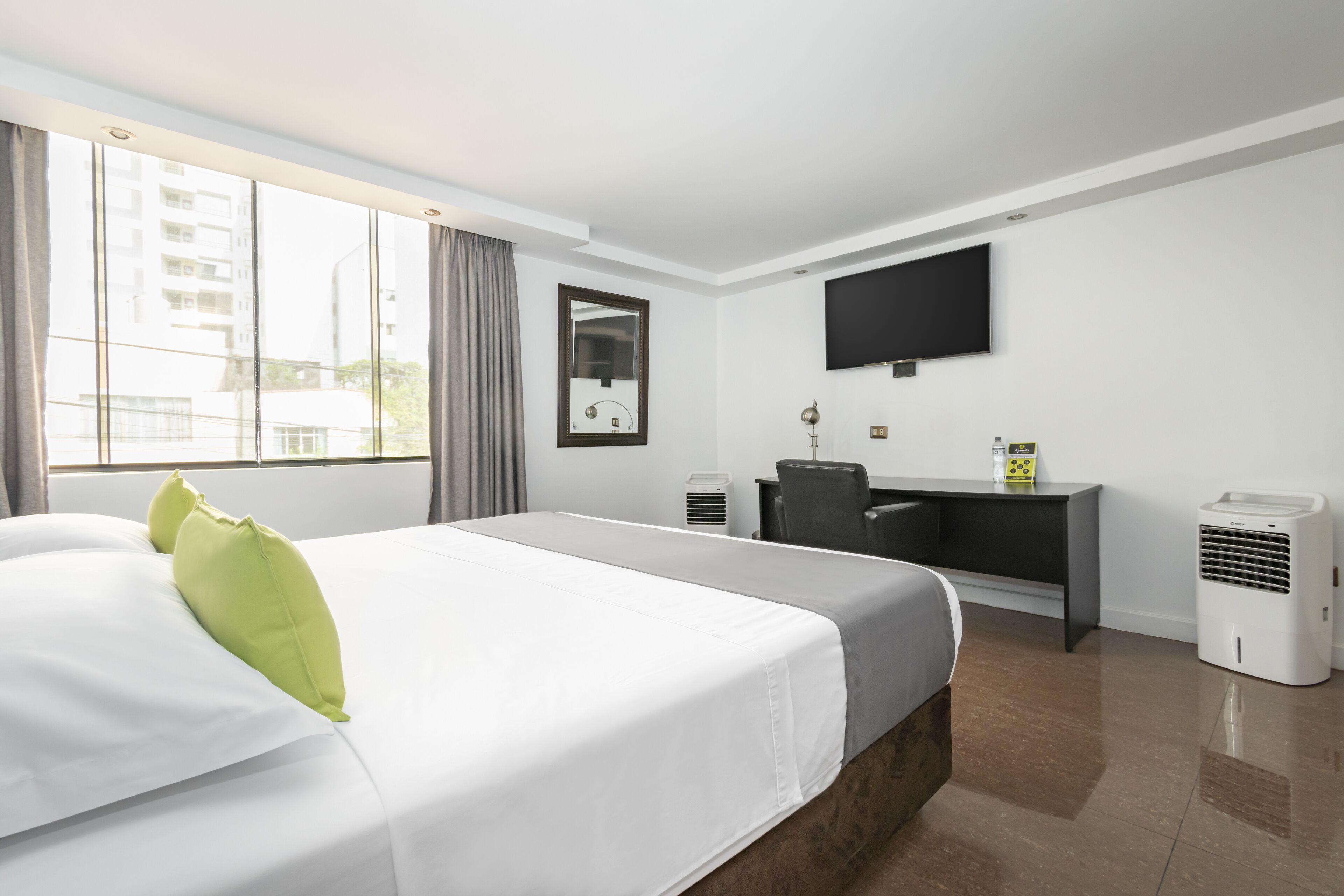 A hotel room with a large bed, a desk, a chair, a flat-screen TV, and two air conditioning units.