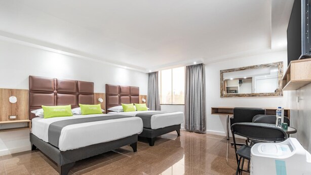 Hotelkamer met twee bedden, een bureau, een stoel, een spiegel en een raam met gordijnen.