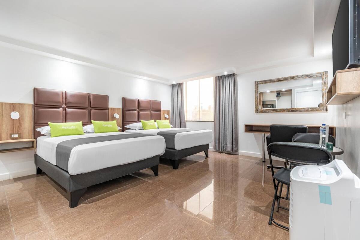 A hotel room with two beds, a desk, a chair, a mirror, and a window with curtains.
