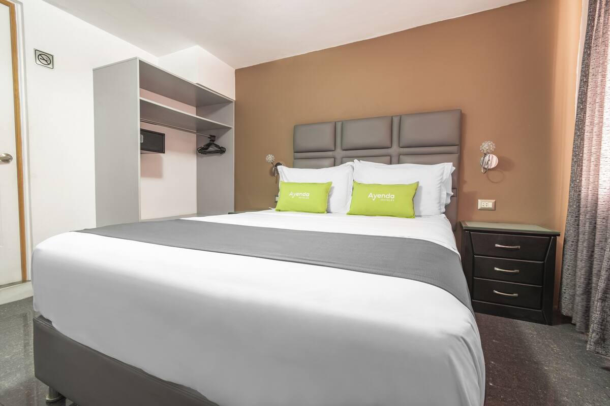 A hotel room with a large bed, a bedside table, a wardrobe, and a wall-mounted light fixture.