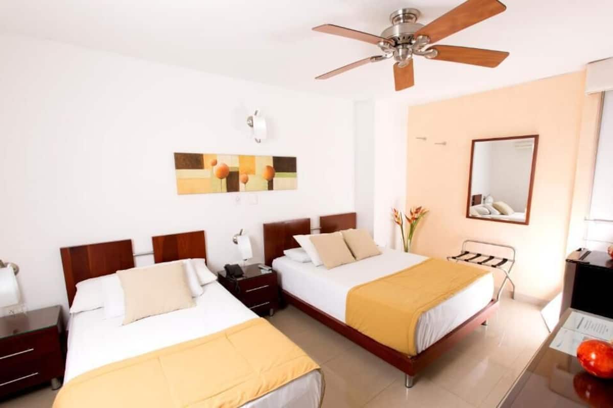 A hotel room with two beds, a ceiling fan, a mirror, and a desk with a lamp.