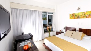 Habitación de hotel con una cama grande, un escritorio con computadora, un televisor y una ventana con cortinas.