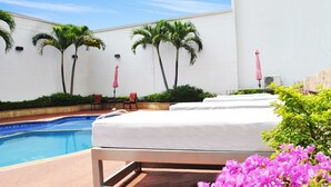Zona junto a la piscina con una cama, palmeras y una piscina.