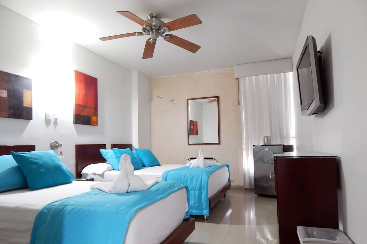 A hotel room with two beds, a ceiling fan, a TV, a mirror, and a small kitchenette.
