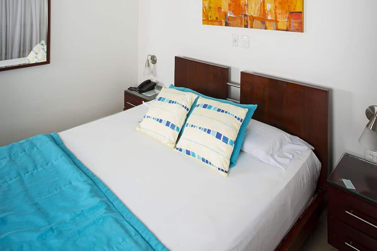 A bedroom with a bed, a ceiling fan, a nightstand, a bedside lamp, and a painting on the wall.