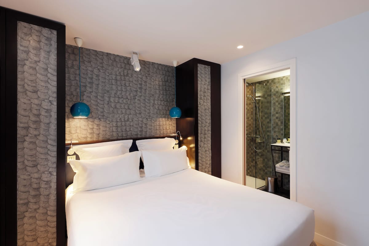 Una habitación de hotel moderna con una cama grande, una pared con textura de piedra y una zona de ducha de vidrio.