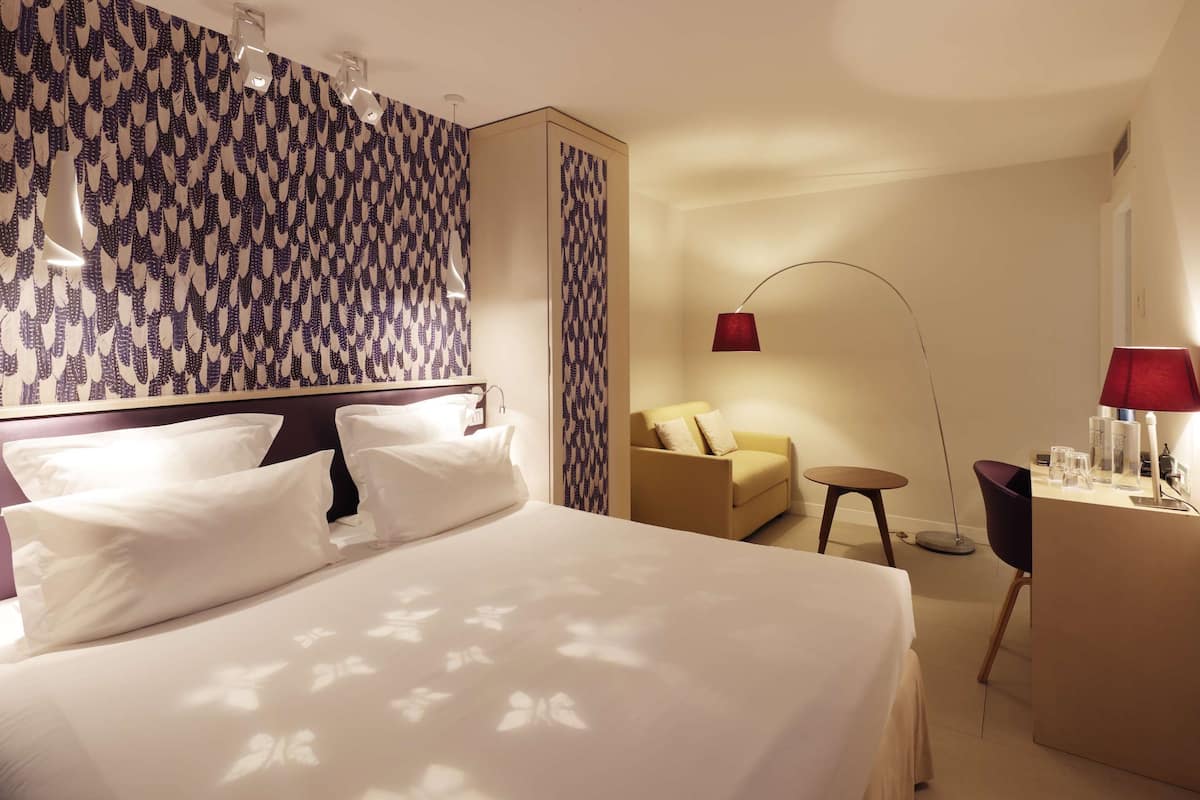 Una habitación de hotel con una cama grande, un sofá, un escritorio y un papel tapiz estampado.