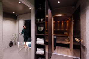 A modern bathroom with a glass partition, wooden shelves with towels, and a mirror. - Hotel Eden (Paris)