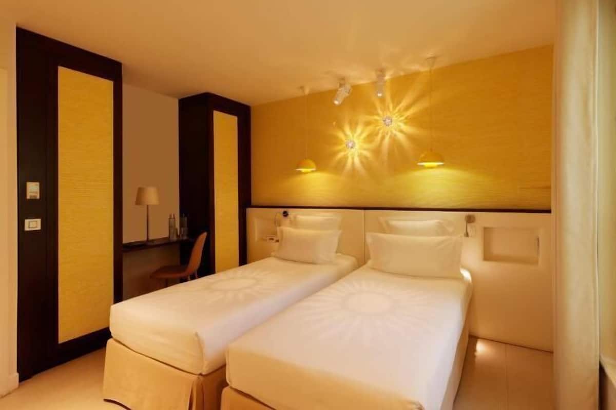 Una habitación de hotel con dos camas individuales, una mesita de noche, una lámpara y un espejo.