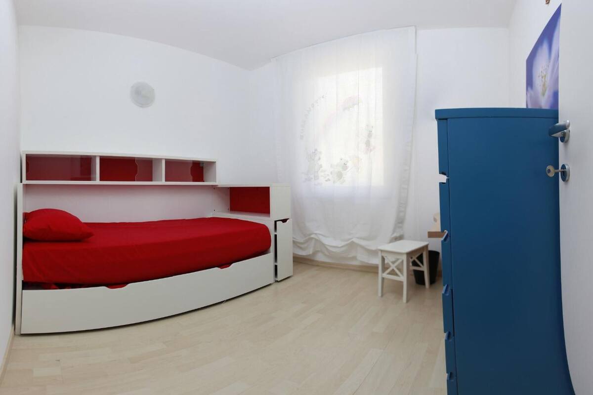 Ein Zimmer mit einem gebogenen Bett, einem kleinen Schreibtisch und einem blauen Schrank.