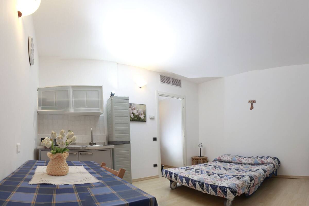 Ein gemütlicher Raum mit Küchenzeile, einem Essbereich inklusive Tisch und Stühlen sowie einem Bett mit Steppdecke.