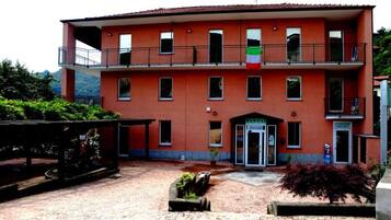 Un edificio a due piani con facciata rossa, un balcone al piano superiore e un piccolo ingresso con un cartello.