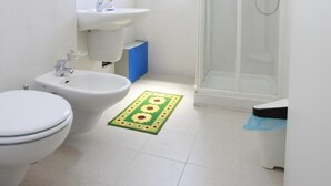 Casa de banho pequena e limpa, com sanita, lavatório e chuveiro.