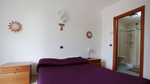 Quarto com cama, mesa de cabeceira, cômoda e banheiro visível por uma porta aberta.