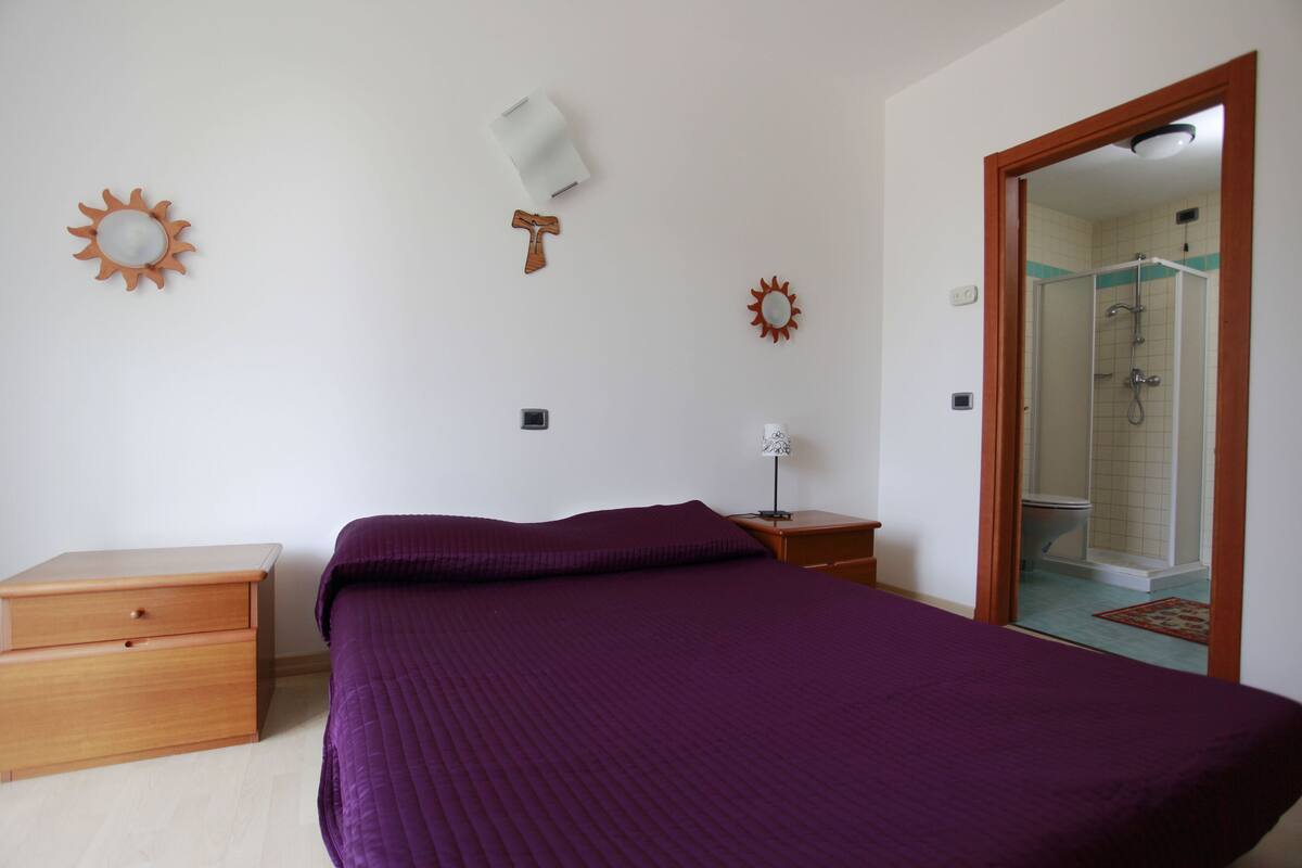 Ein Schlafzimmer mit einem Bett, einem Nachttisch, einer Kommode und einem durch eine offene Tür einsehbaren Badezimmer.