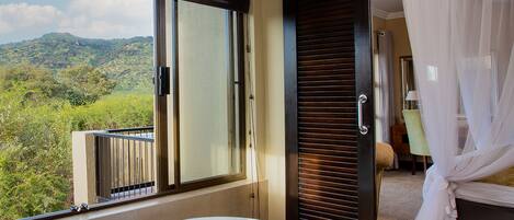 Un baño con una bañera grande, una puerta corrediza de vidrio que da a un balcón y una cama con dosel.