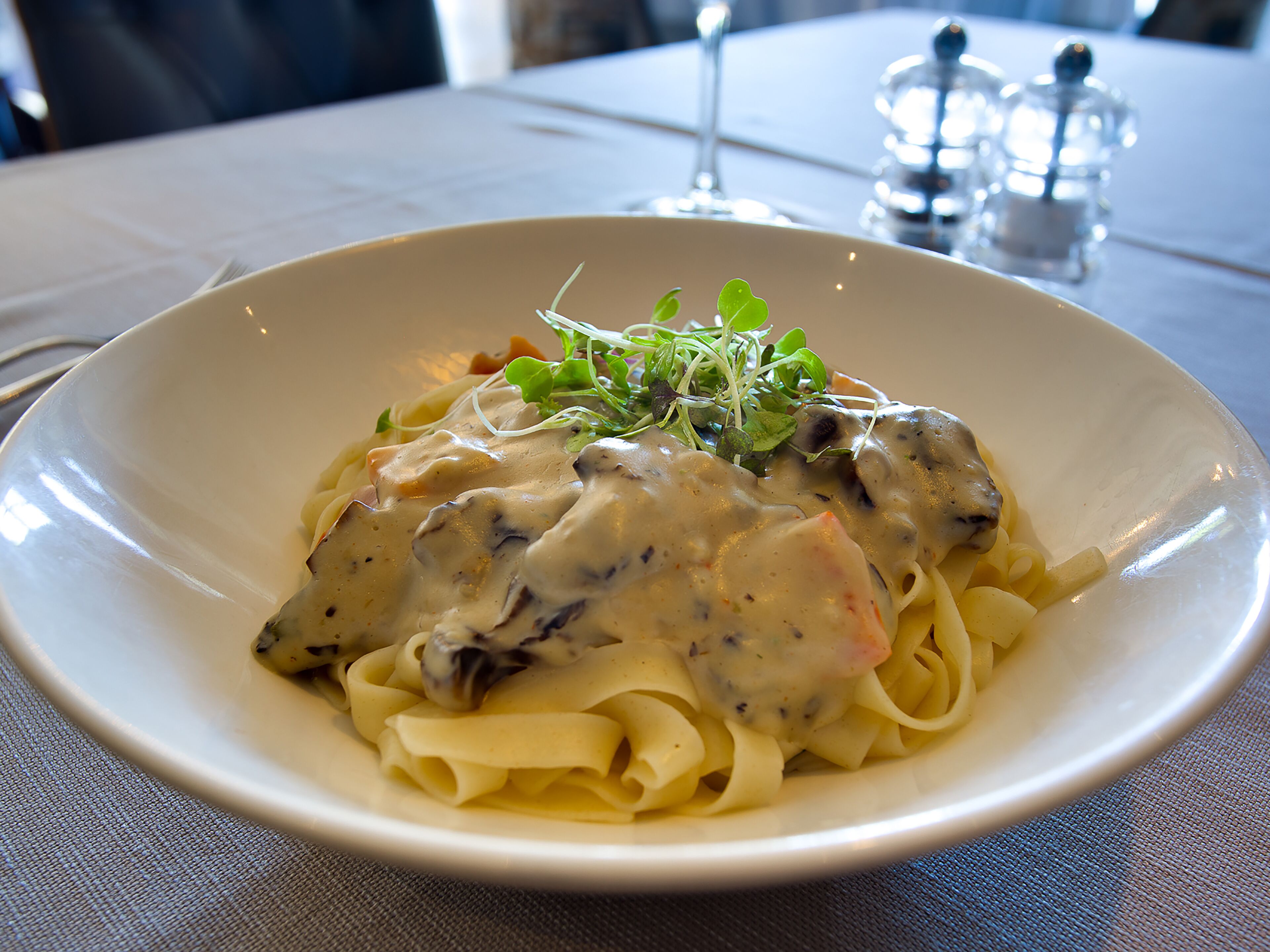 Un plato de pasta cremosa con champiñones, adornado con vegetales verdes, servido sobre un plato blanco.
