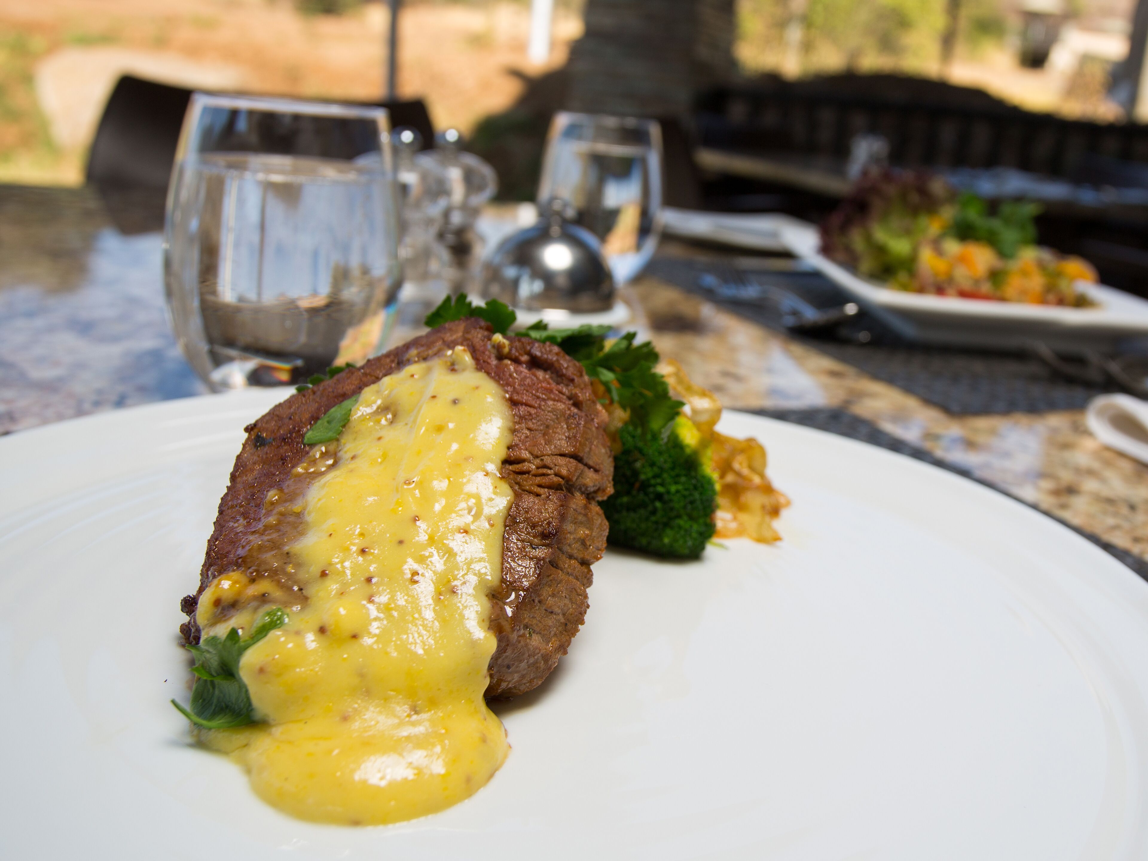 A steak with sauce on a plate, a glass of water, and a fork on a table.
