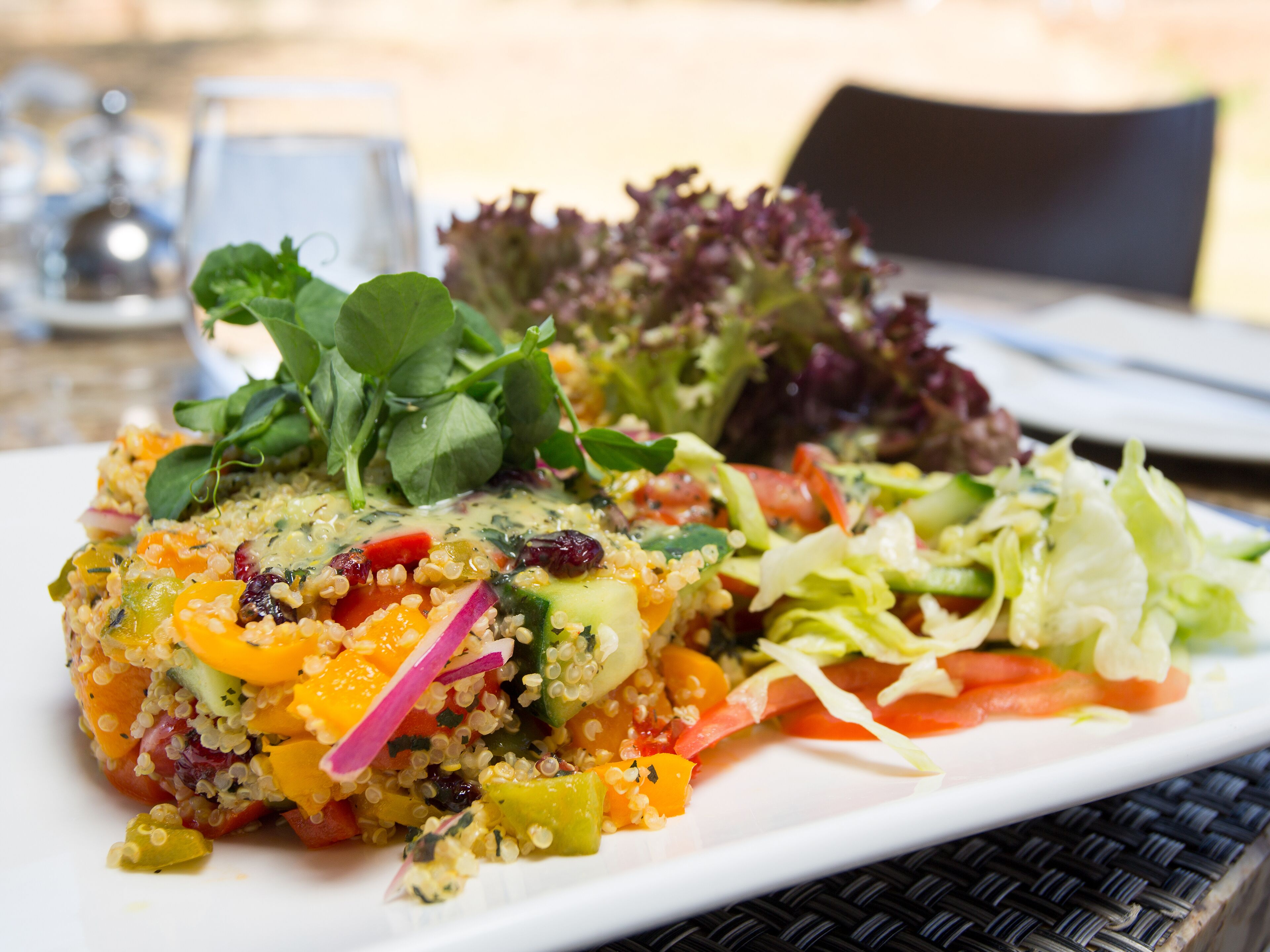 A plate of quinoa salad with vegetables and greens, accompanied by a side of mixed greens and a small salad.
