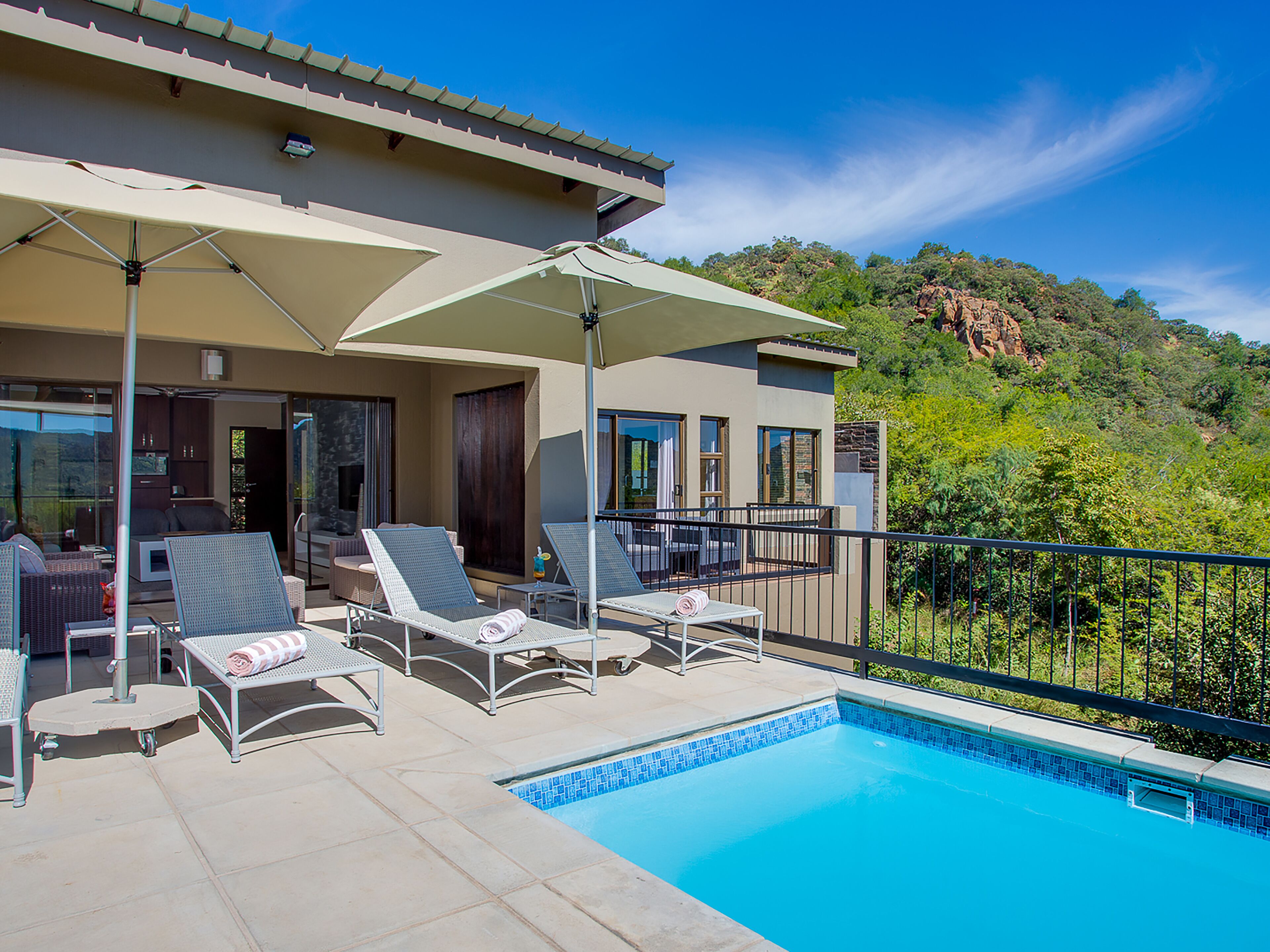 Un espace aménagé au bord de la piscine, avec des chaises longues et des parasols, une piscine et une vue sur un paysage montagneux.