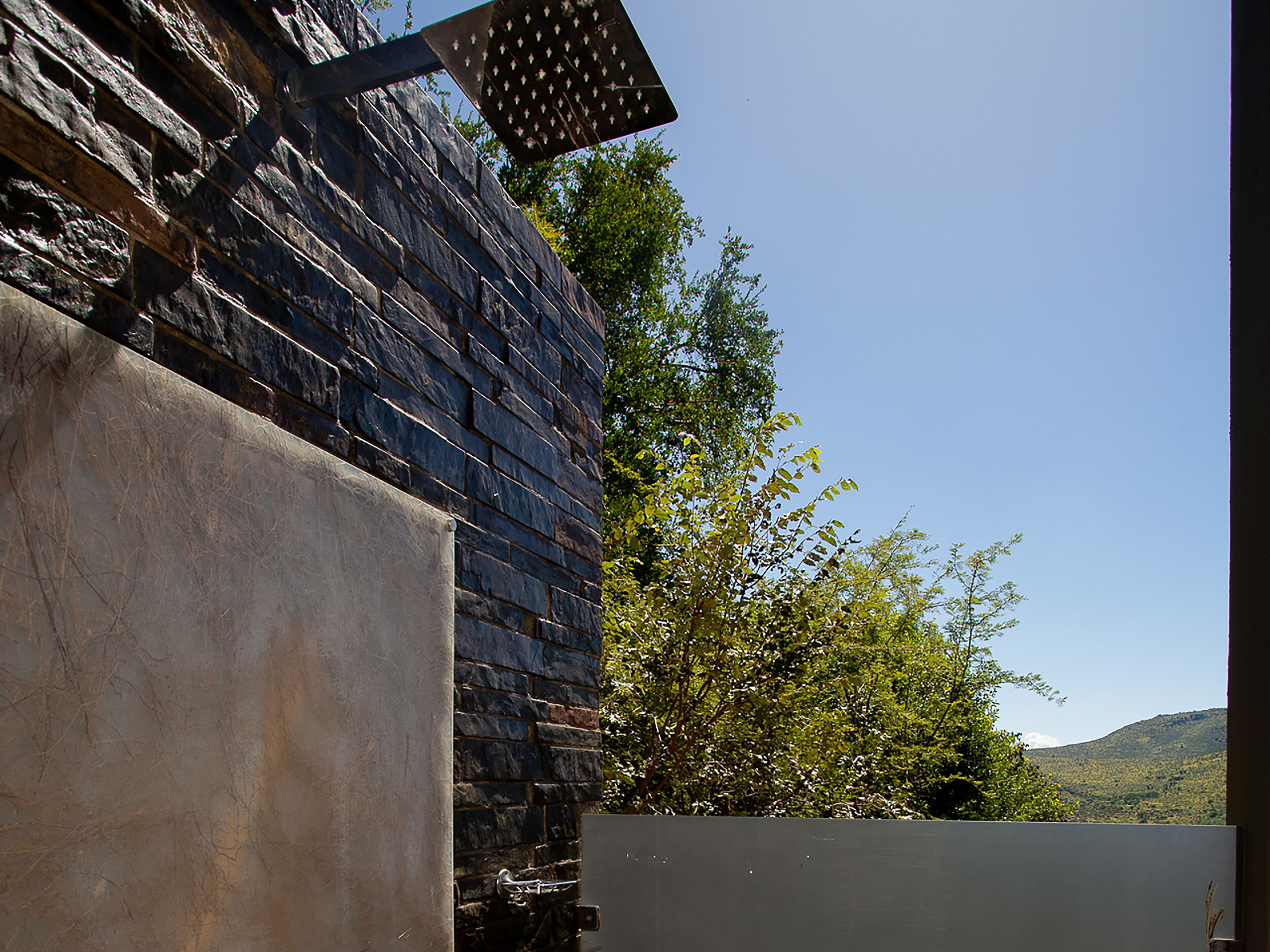 A stone building with a metal awning and a view of green trees and hills in the background.