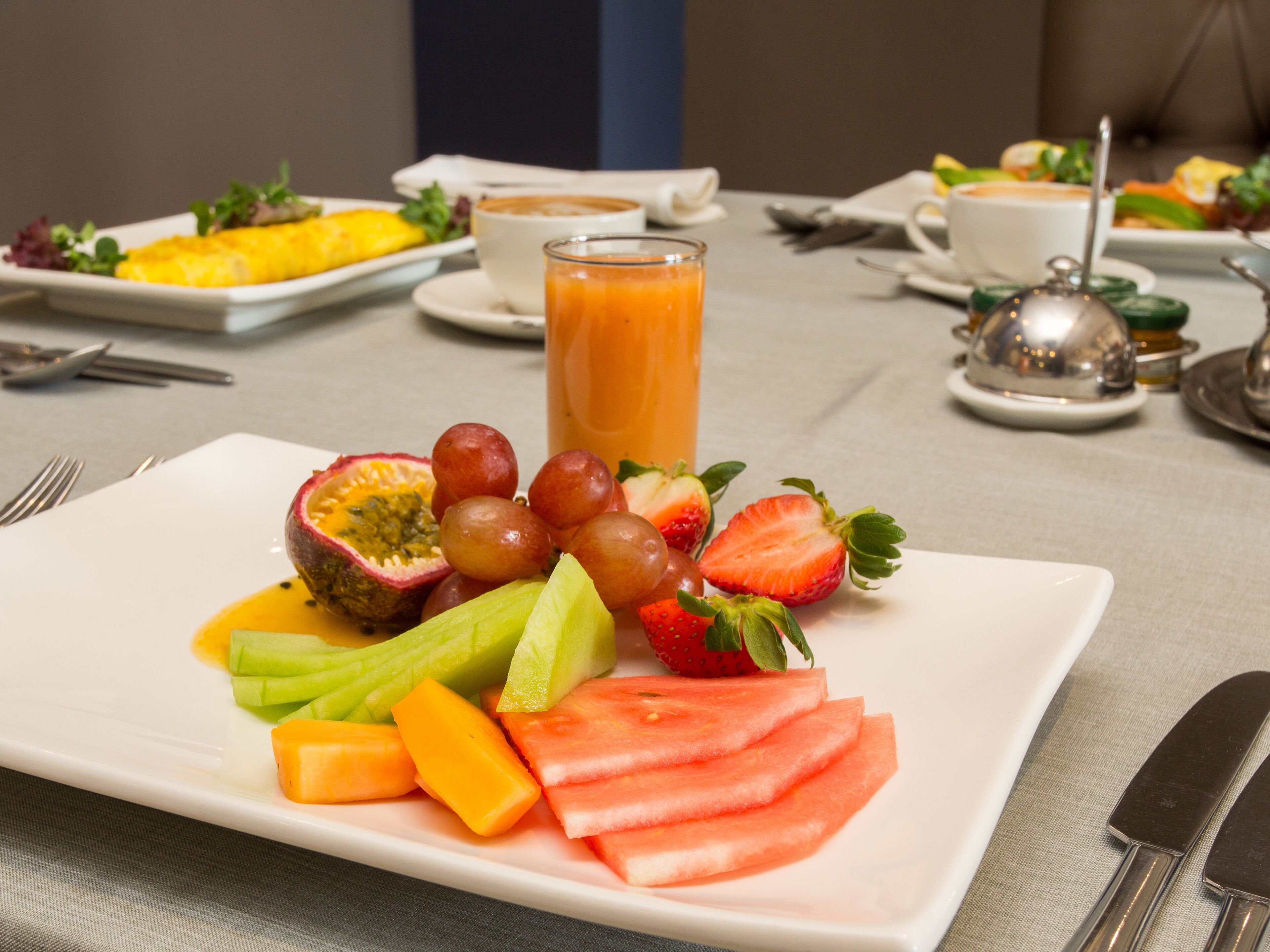 Ein Frühstückstisch mit einer Schüssel frischem Obst, einem Glas Orangensaft und einer Tasse Kaffee.