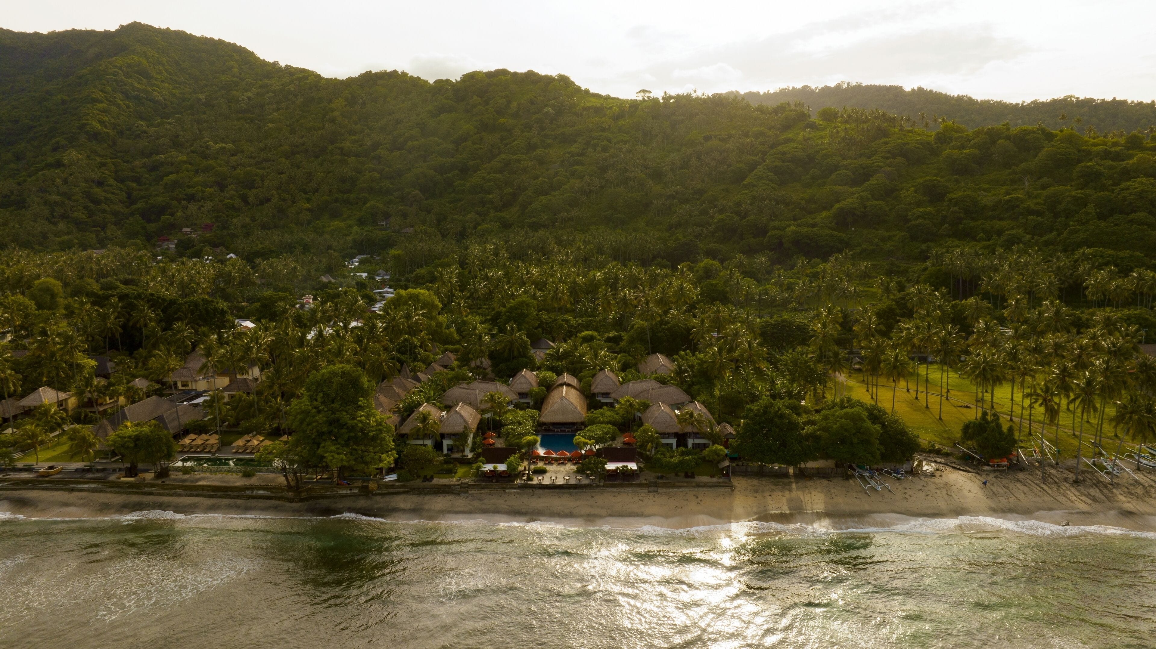 A coastal resort with thatched-roof bungalows, a swimming pool, and a beach.