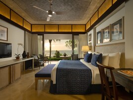 Habitación de hotel con una cama grande, un escritorio con televisor, un balcón con vista al océano y un ventilador de techo.