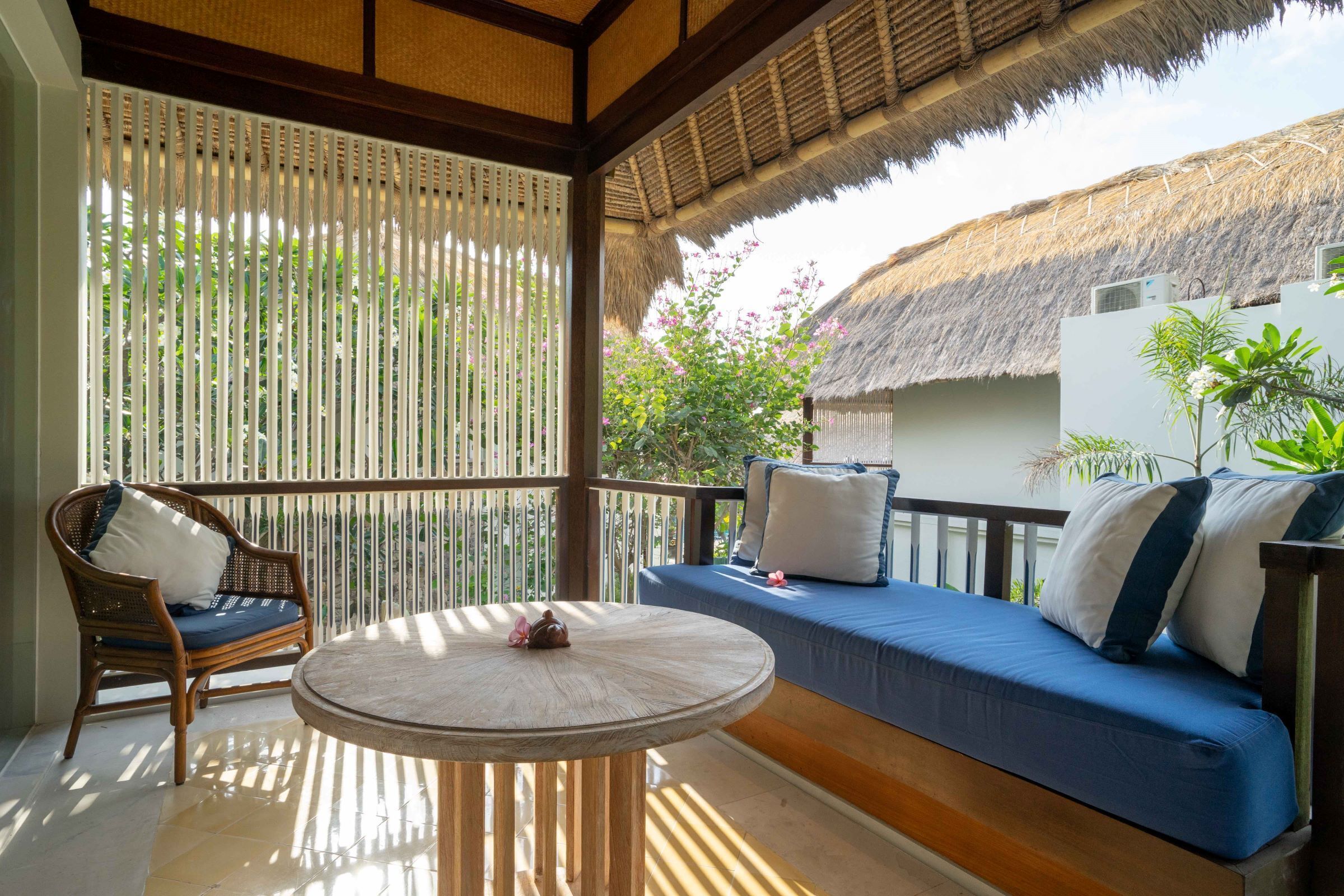 A balcony with a wooden table, a wicker chair, and a blue sofa with pillows.