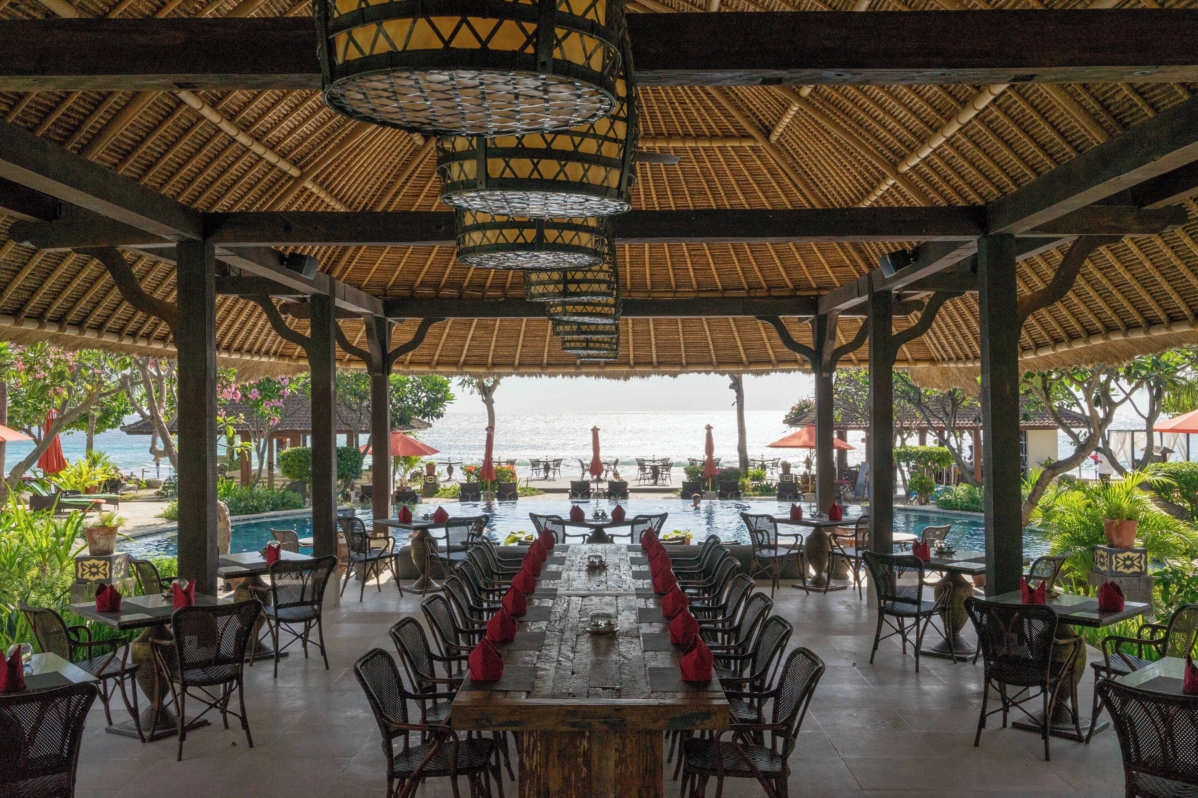 Un área de comedor al aire libre con una mesa larga y sillas, con vista a una piscina y al mar.