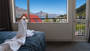 Quarto de hotel com uma cama, uma janela com vista para as montanhas e uma porta com varanda.