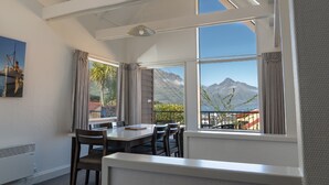 Uma área de refeições com mesa e cadeiras, janelas amplas com vista para as montanhas e teto com claraboias.