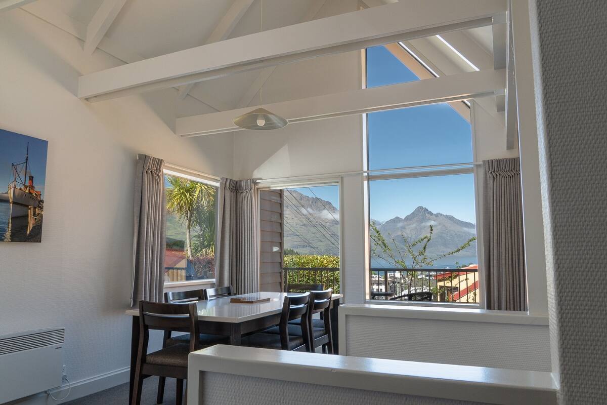 A dining area with a table and chairs, large windows with mountain views, and a ceiling with skylights.