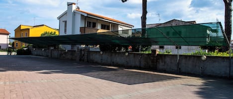Un'area esterna pavimentata con una struttura a tetto verde, un edificio bianco con tetto rosso e un edificio giallo sullo sfondo.