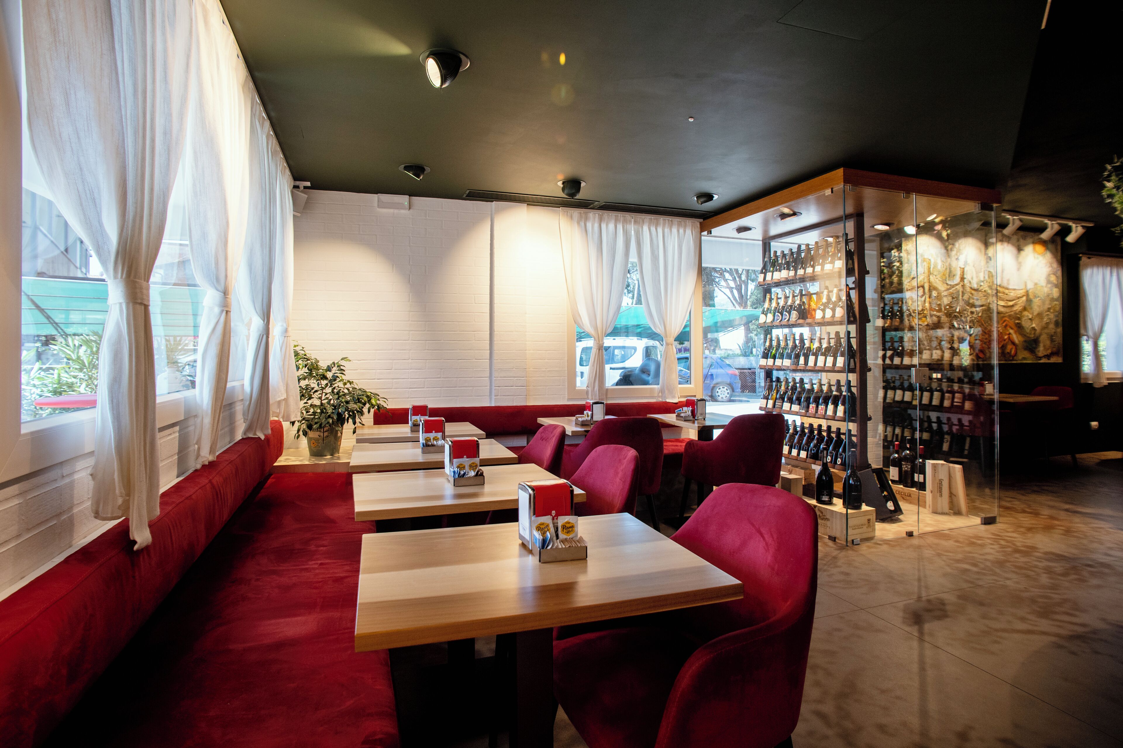 A restaurant with red cushioned seating, wooden tables, and a wine display.