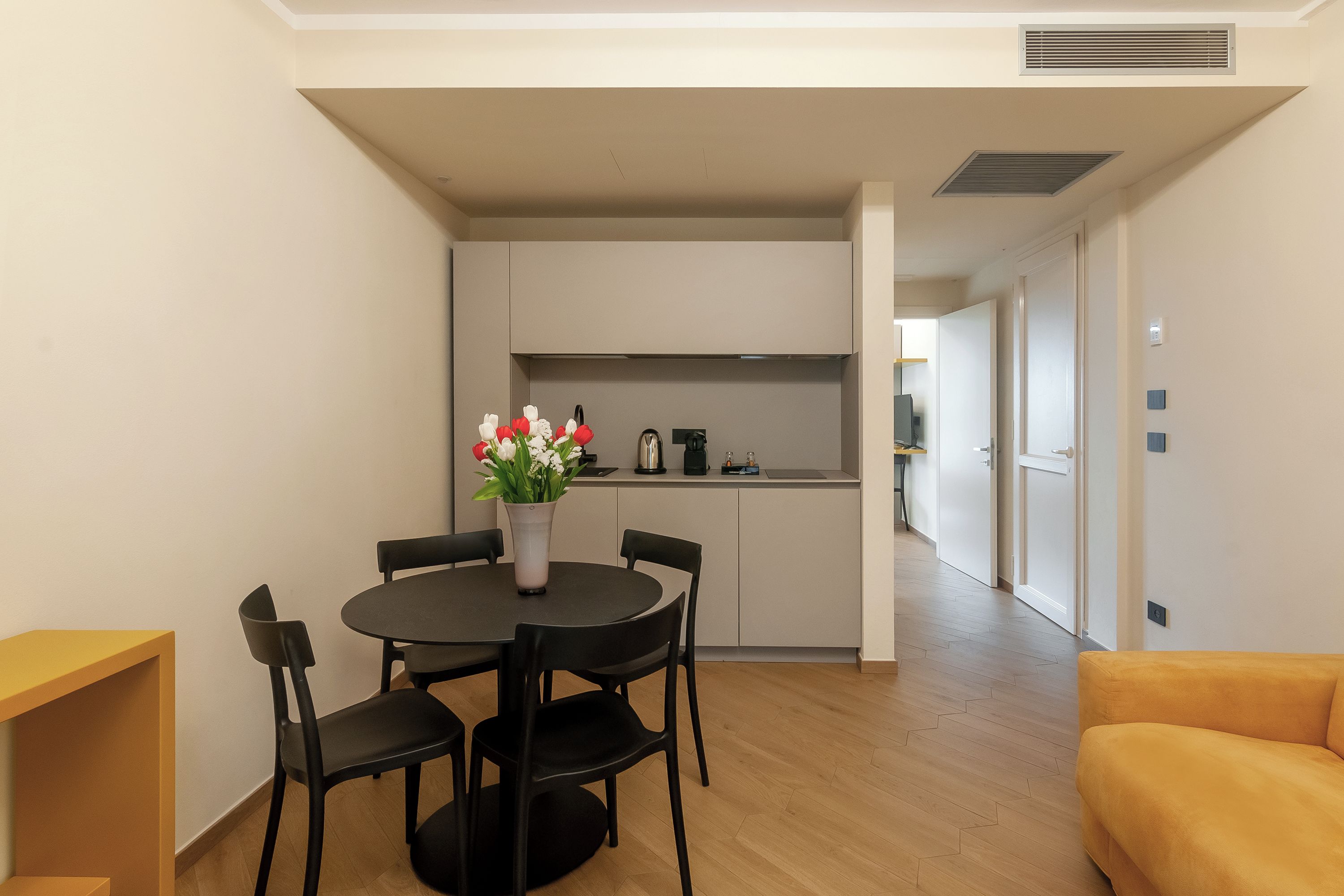 Une cuisine moderne avec un coin repas, une machine à café et un vase rempli de fleurs sur la table.