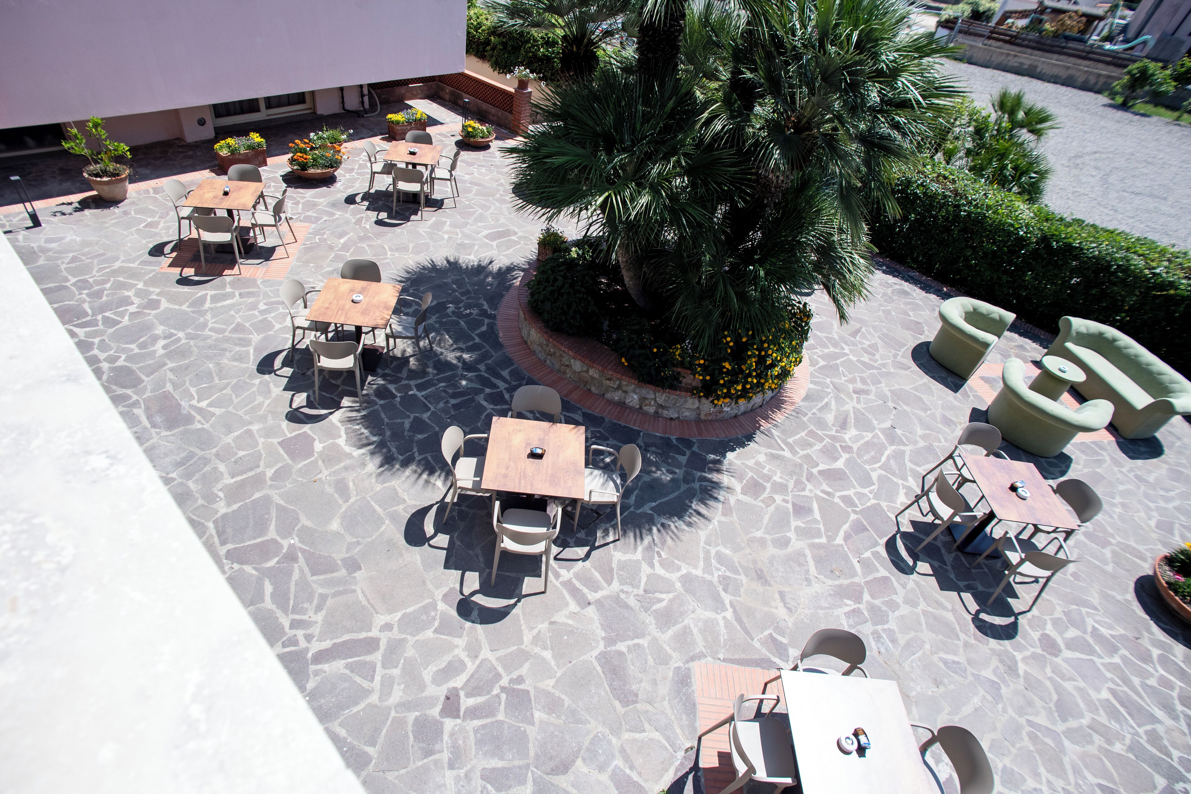 Un patio al aire libre con suelo de piedra, varias mesas y sillas, y plantas en macetas.