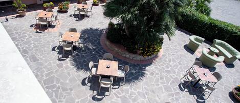 An outdoor patio area with stone flooring, multiple tables and chairs, and potted plants.