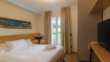 Habitación de hotel con cama, un cuadro en la pared, televisor y ventana con cortinas.