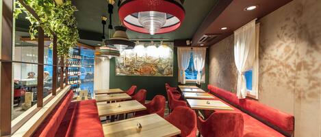 A restaurant interior with red upholstered booths, wooden tables, and hanging pendant lights.