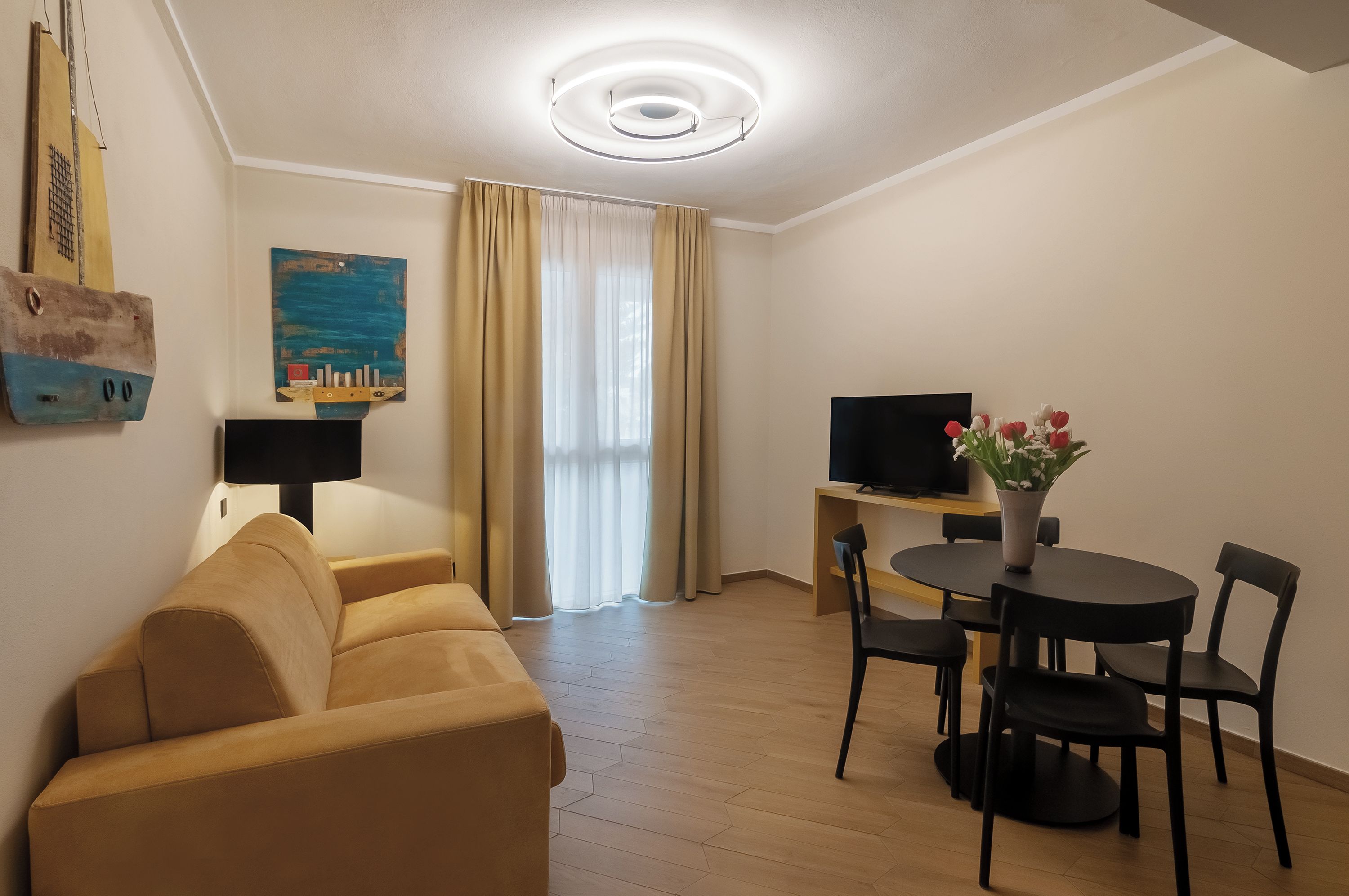 A modern living room with a sofa, a television, a dining table with chairs, and a painting on the wall.
