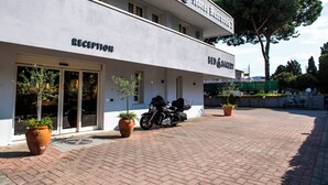 Une réception d’hôtel avec une pancarte indiquant « chambre et petit-déjeuner », une moto garée à l’extérieur et des plantes en pot.