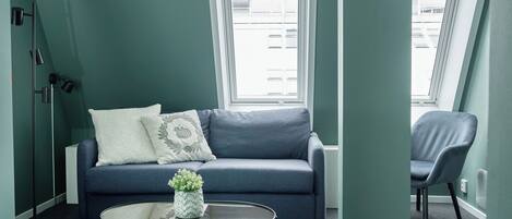 A modern living room with a blue sofa, a round glass coffee table, and a potted plant.