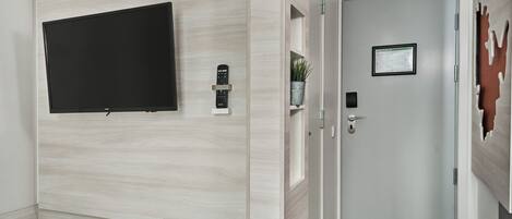 Ein Hotelzimmer mit einem an der Wand befestigten Fernseher, einer Tür mit Schlüsselkarten-Schließung, einer kleinen Pflanze und einem gerahmten Dokument.