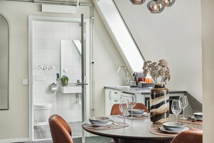 A modern kitchen with white cabinets, a dining area with a round table set for two, and a large window above the sink.