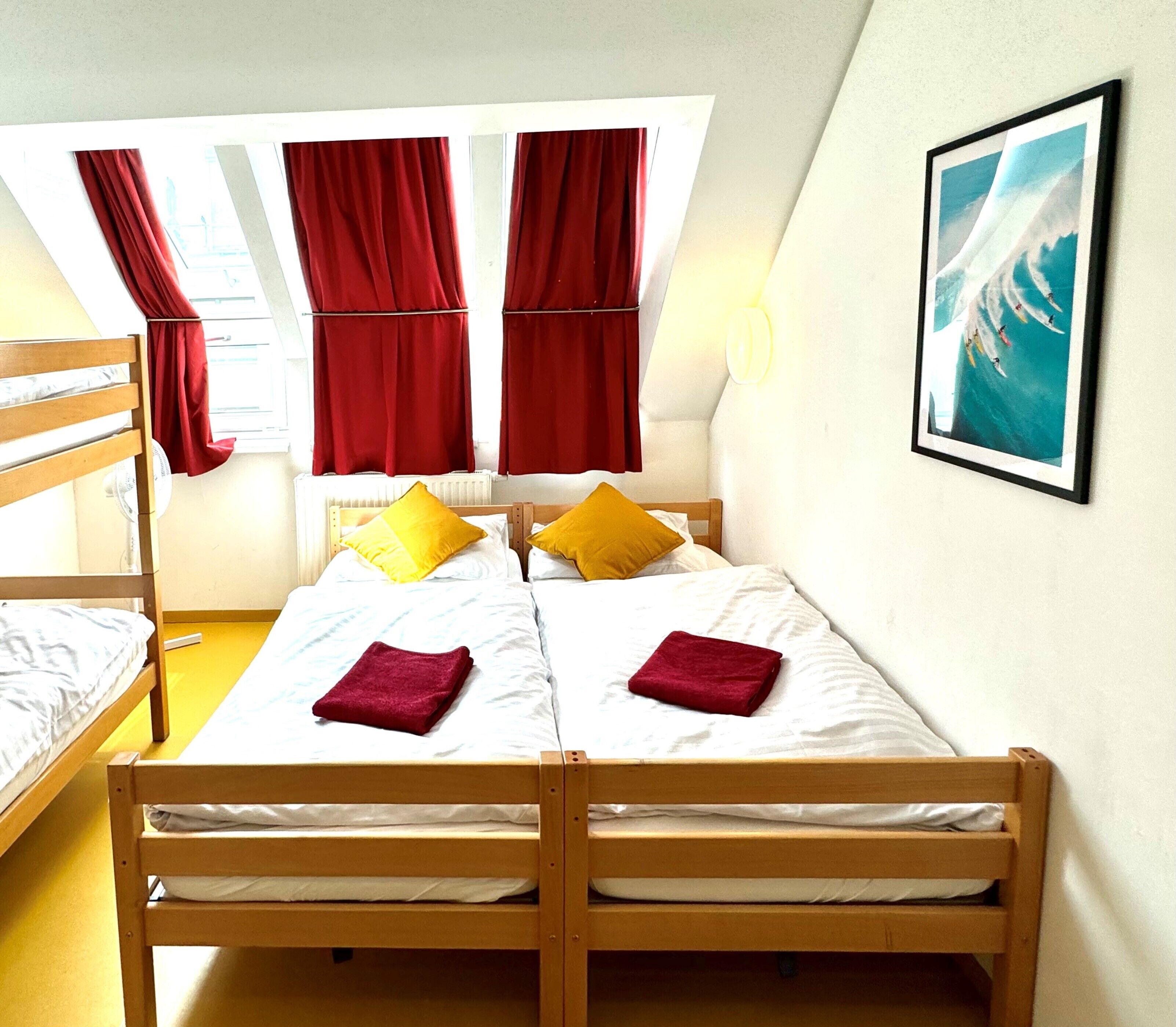 A room with two wooden beds, red curtains, a white radiator, and a framed picture on the wall.